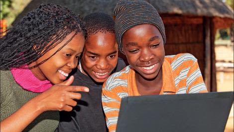 Three teenage girls looking at a laptop smiling.