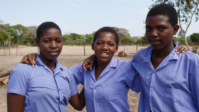 Image shows three teenage girls embraced smiling at the camera.