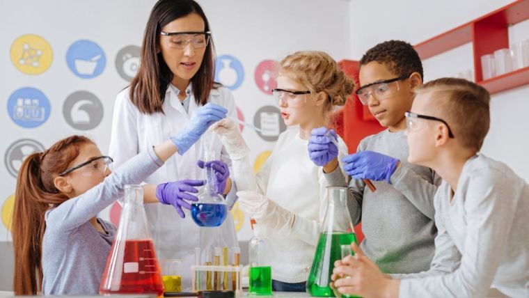 Group of teenage students and female teacher in science lesson, mixing chemicals