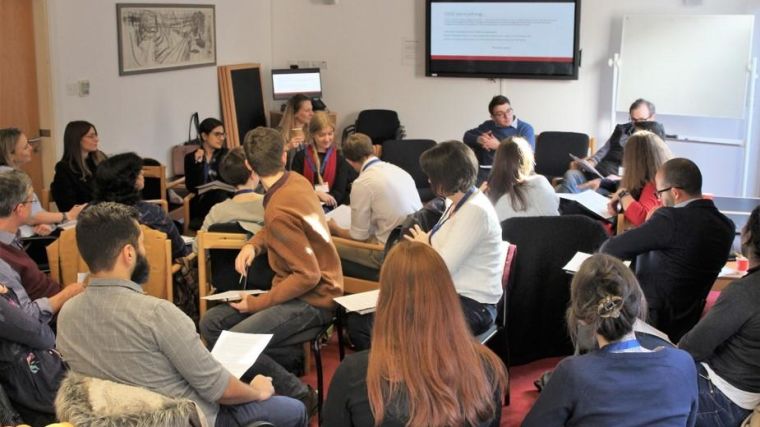 Image shows group of participants sat down, listening to a speaker at the front of the room leading the course.