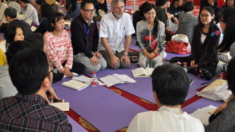 Group of people, kneeling in a circle, in the centre are yoga mats and notebooks.