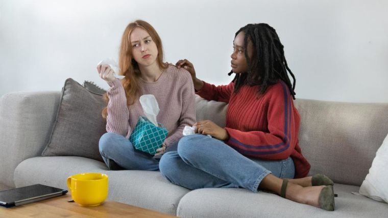 Two friends sit on a sofa and console each other