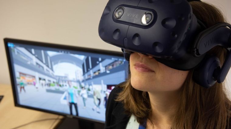 Woman wearing a virtual reality headset next to a computer screen