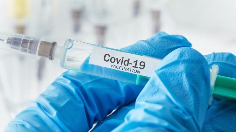 Syringe with COVID-19 vaccine label held in gloved hand