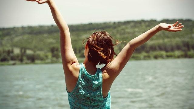 Woman looking over water with arms up in their air