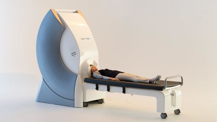 image shows patient lying on a bed with their head being scanned by a large machine.