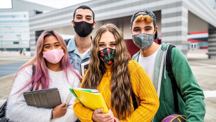 4 young people wearing face masks with school books/bags standing together