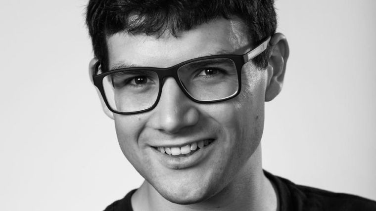 Headshot of Alexander, male smiling at camera wearing glasses